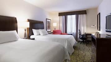 A hotel room with two beds, a desk, a chair, a television, and a window with curtains.