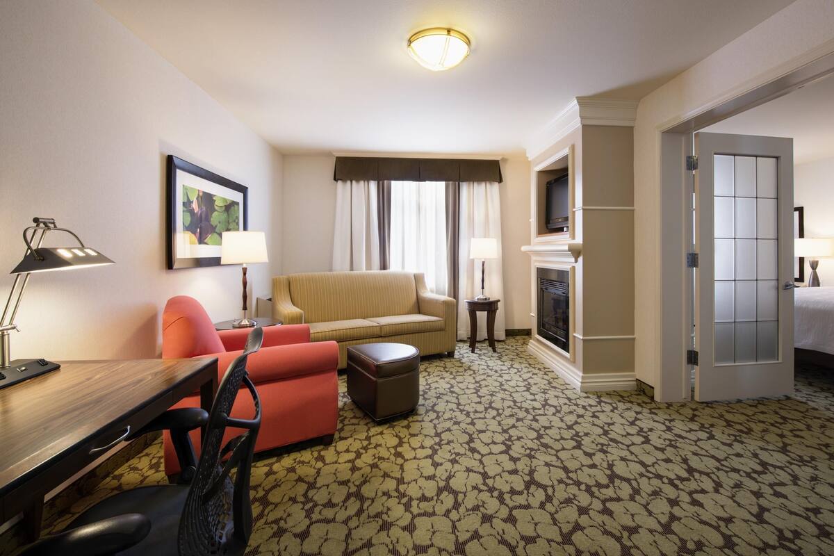 A hotel room with a sofa, armchair, desk, and a television.