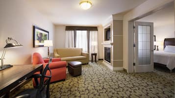 A hotel room with a sofa, armchair, desk, and a television.
