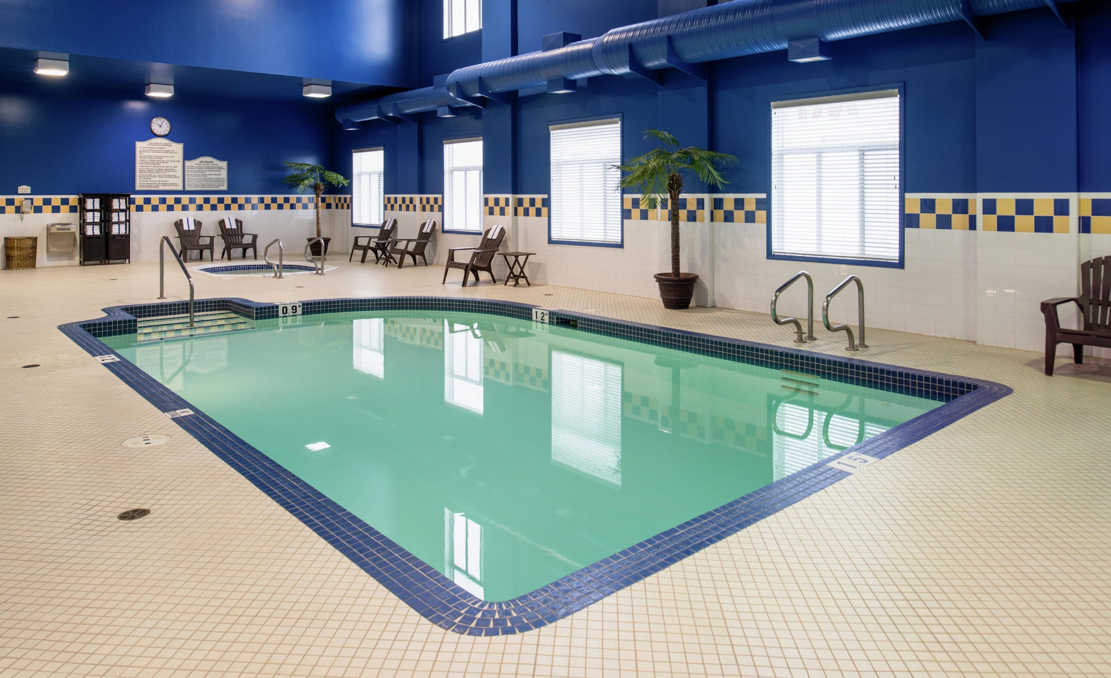 Una piscina interior con agua cristalina, rodeada por un suelo y paredes de azulejos, con un reloj y señalización informativa en las paredes.