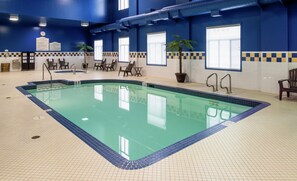 An indoor swimming pool with clear water, surrounded by a tiled floor and walls, with a clock and informational signs on the walls. - Hilton Garden Inn West Edmonton (Edmonton)