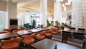 Un comedor de hotel espacioso con varias mesas y sillas, un televisor y una variedad de plantas y elementos decorativos.