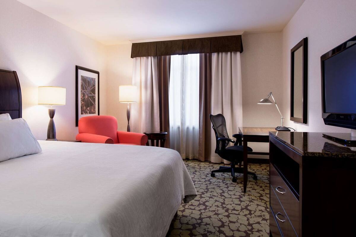 A hotel room with a bed, a desk, a chair, a television, and a window with curtains.