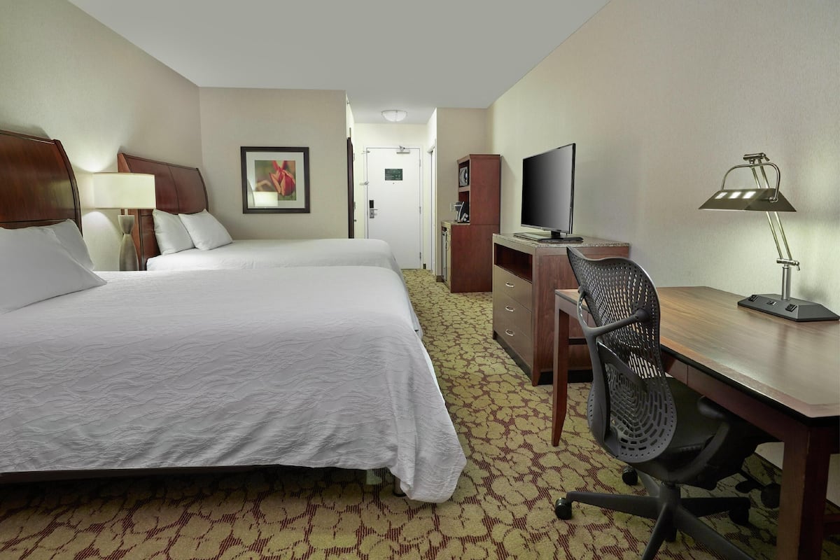 A hotel room with a bed, desk, chair, television, and a lamp.