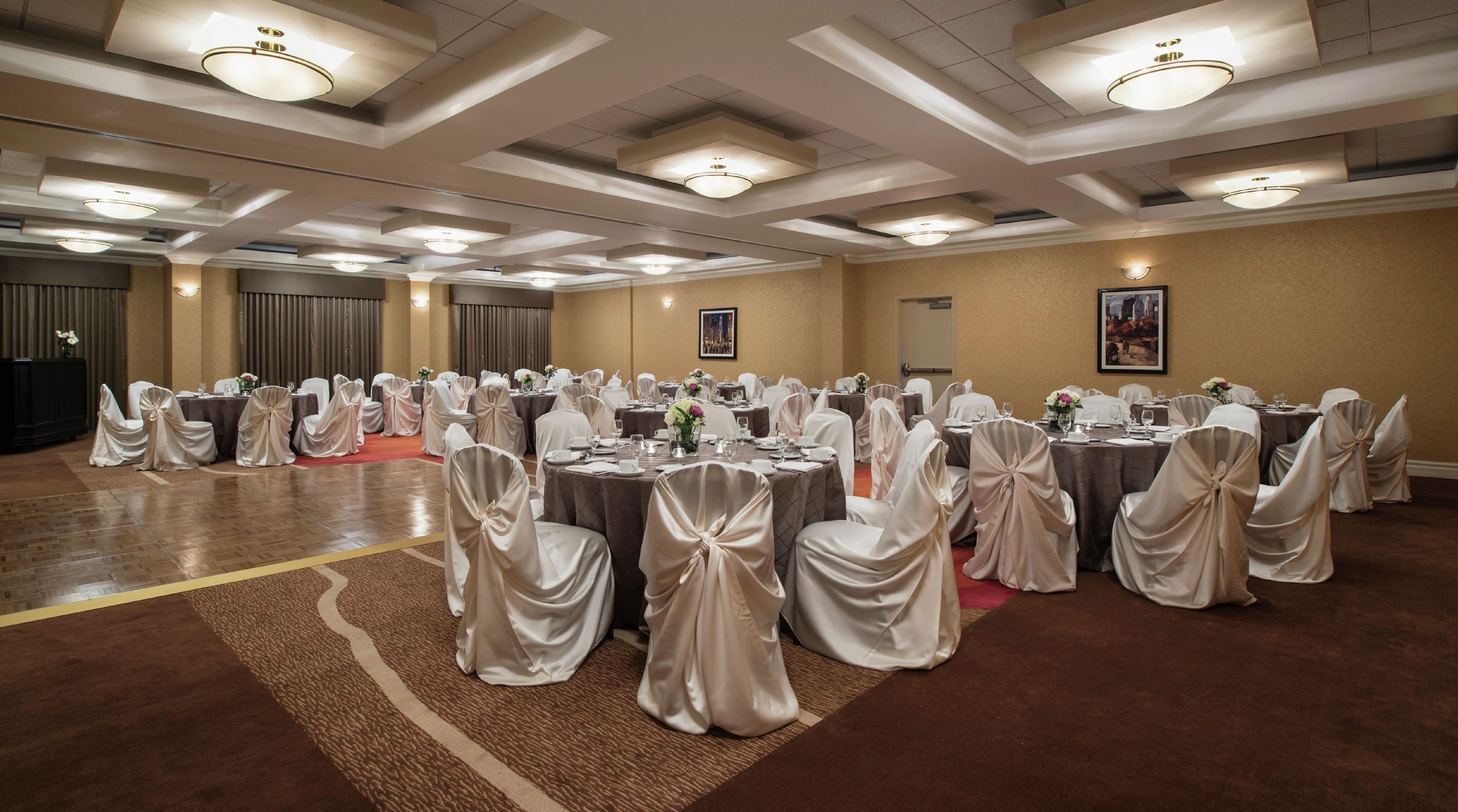 Un salón de banquetes con mesas redondas, sillas con fundas blancas e iluminación empotrada.