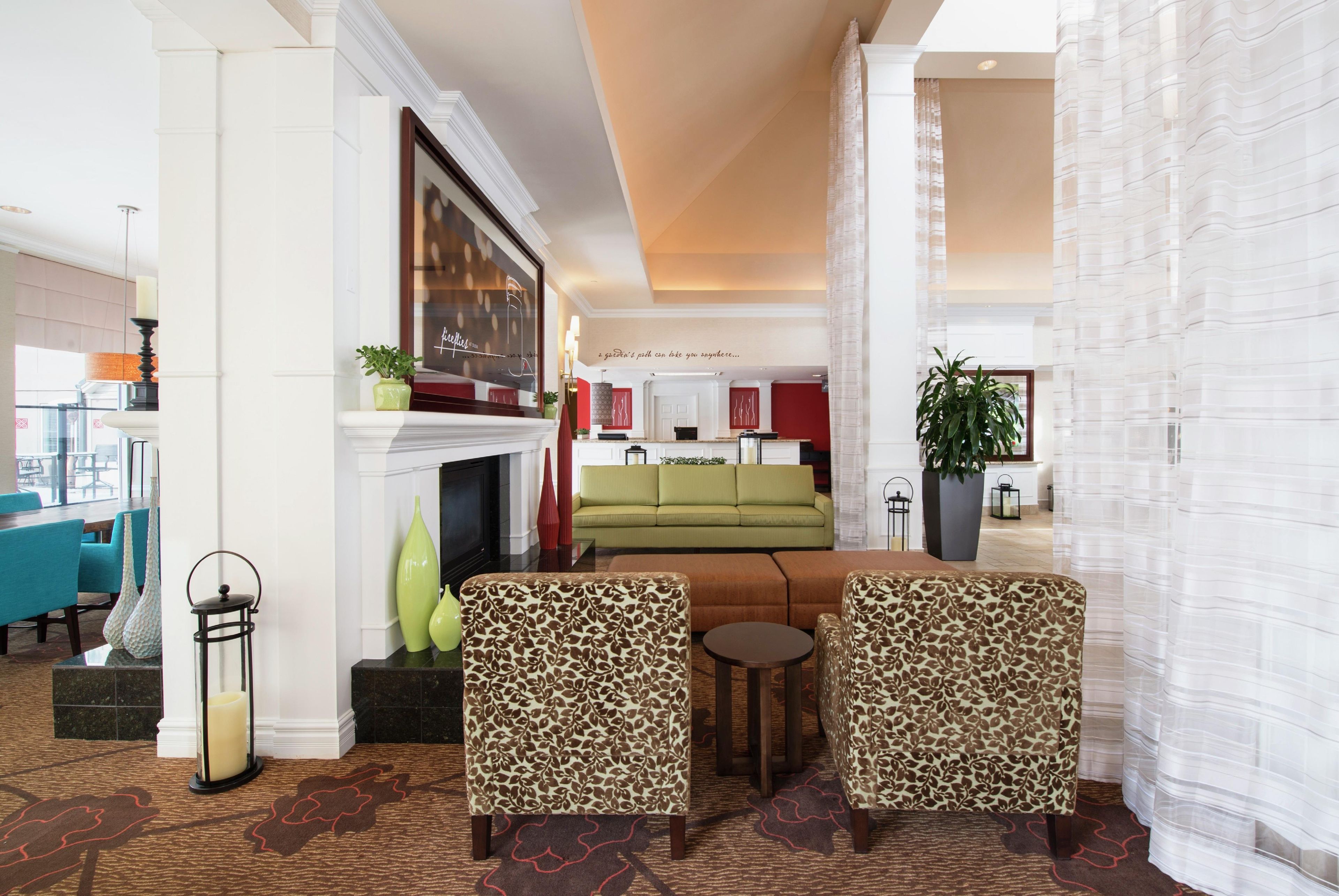 A hotel lobby with a fireplace, green sofa, leopard print armchairs, and a dining area.