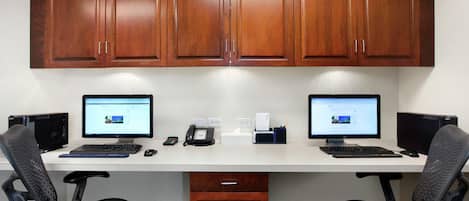Un espacio de trabajo con dos monitores, un escritorio, sillas y armarios de madera.