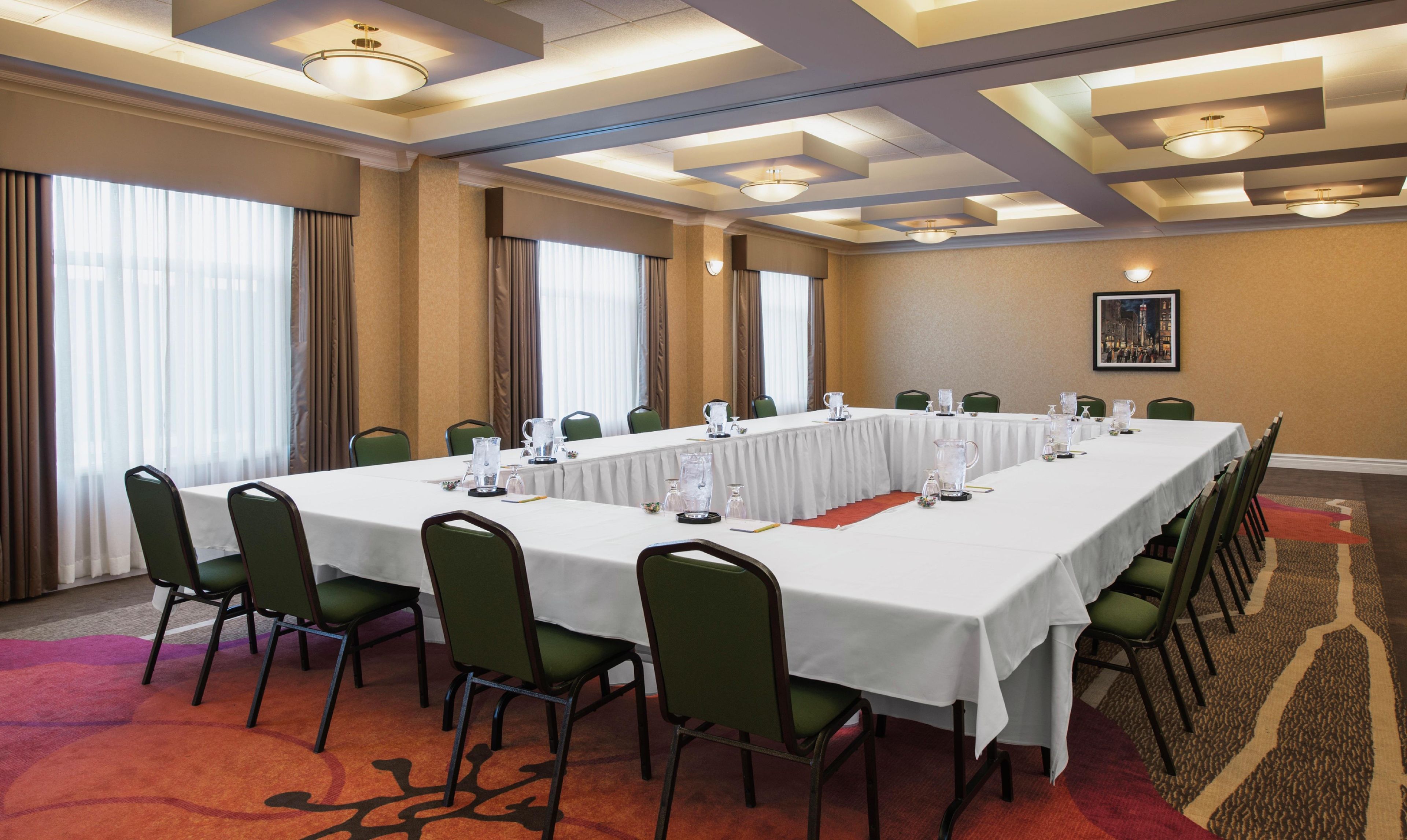 A conference room with a long table, green chairs, and a carpeted floor.