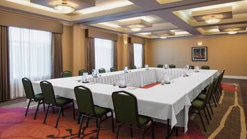 Un salón de conferencias con una mesa larga, sillas verdes y suelo alfombrado.