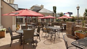 Un patio al aire libre con mesas y sillas, sombrillas rojas y vistas a un edificio con el letrero 'Garden Inn'.