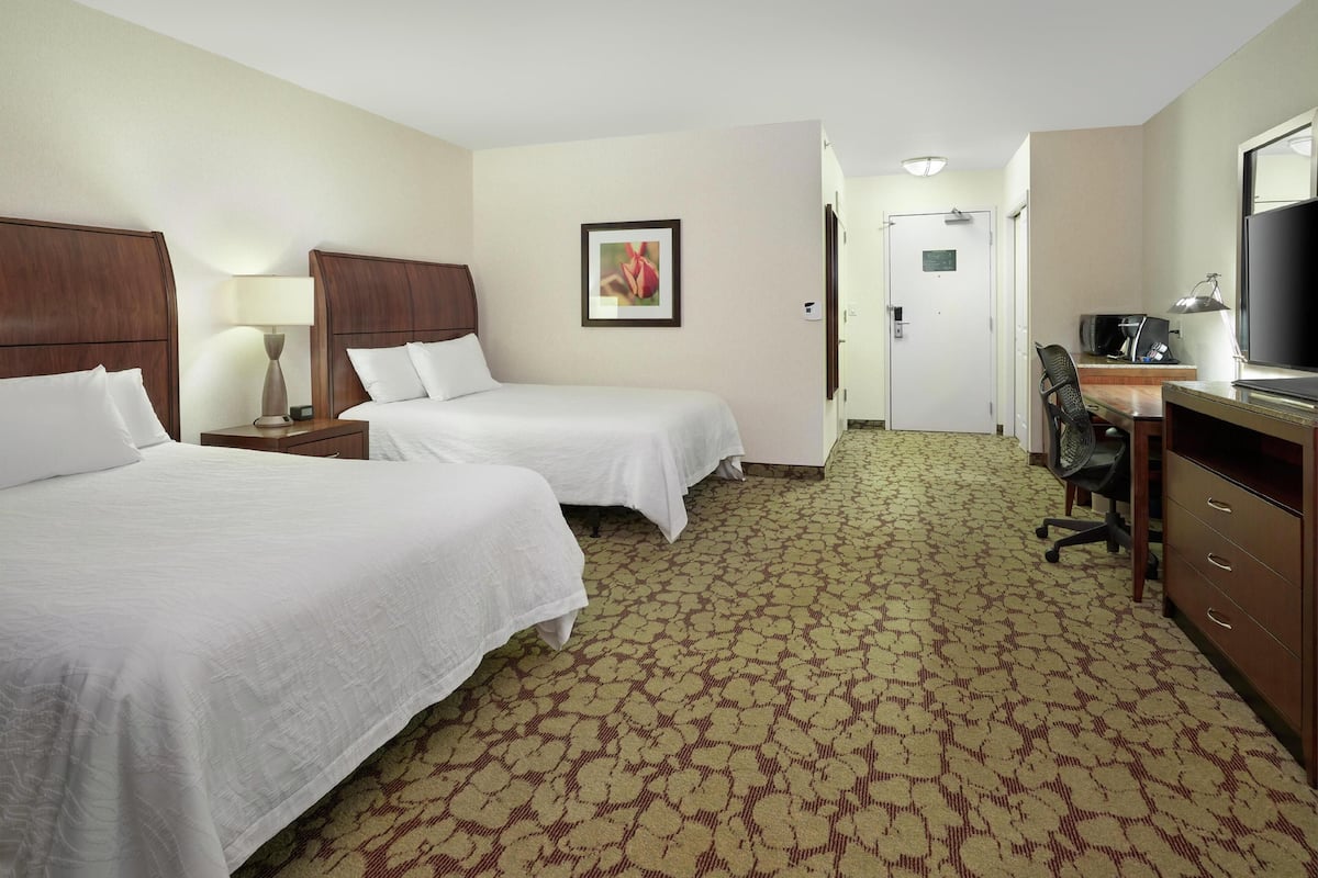 A hotel room with two beds, a desk with a computer, a chair, and a television.