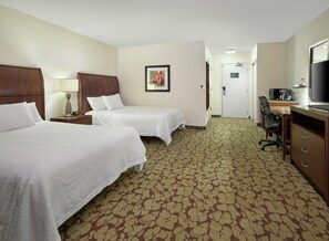 Una habitación de hotel con dos camas, un escritorio con computadora, una silla y un televisor.