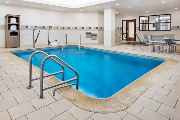 Una piscina con una escalera metálica, un perchero y una mesa con sillas.