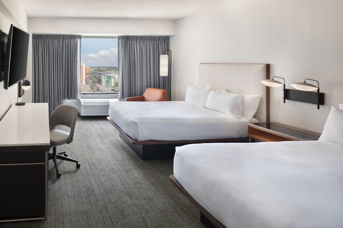 A hotel room with two beds, a desk, a chair, a TV, and a window with curtains.