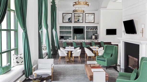 A modern hotel lobby with green and white furniture, a fireplace, and a bar area with a mirrored wall.