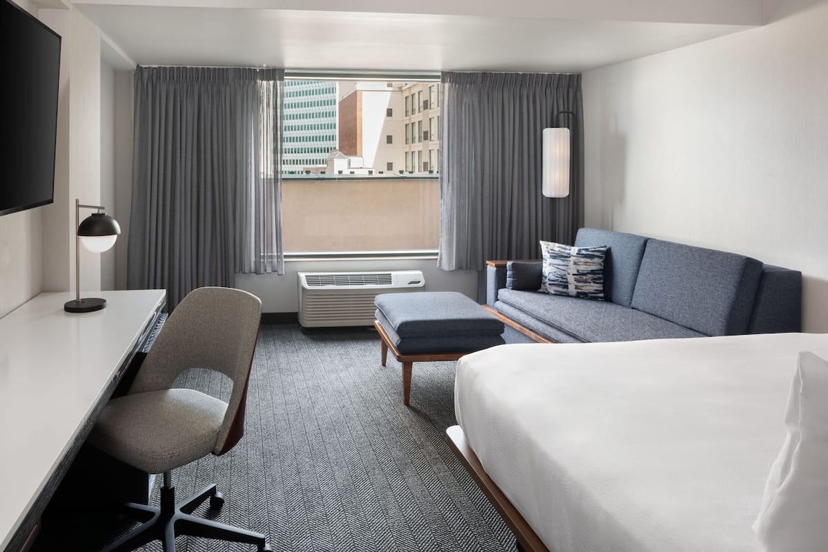 Een hotelkamer met een bed, een bureau, een stoel, een bank en een groot raam met gordijnen.