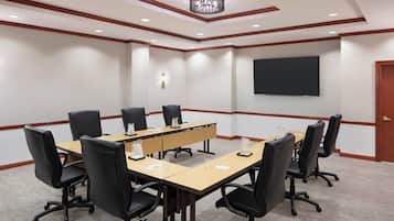A conference room with a long table, black chairs, a projector screen, and a chandelier.