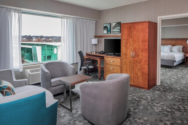Habitación de hotel con escritorio, dos sillas, armario, cama y vista a un edificio.