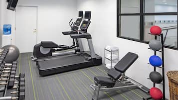 A gym with treadmills, a bench, dumbbells, and exercise balls.