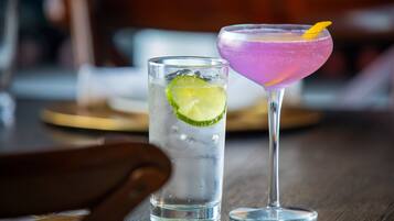 Two drinks on a wooden table, one in a tall glass and one in a martini glass, with a lime wedge in the tall glass.