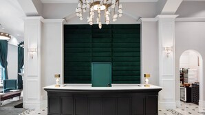 A reception area with a dark wood counter, a green upholstered wall, and a chandelier.