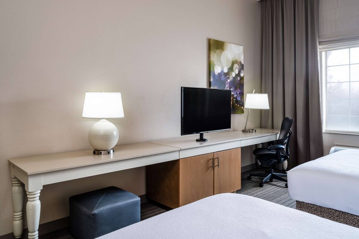 A hotel room with a bed, a desk with a computer, a chair, and a TV.
