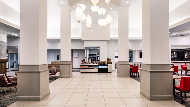 A spacious lobby with a central reception desk, red chairs, and a tiled floor.