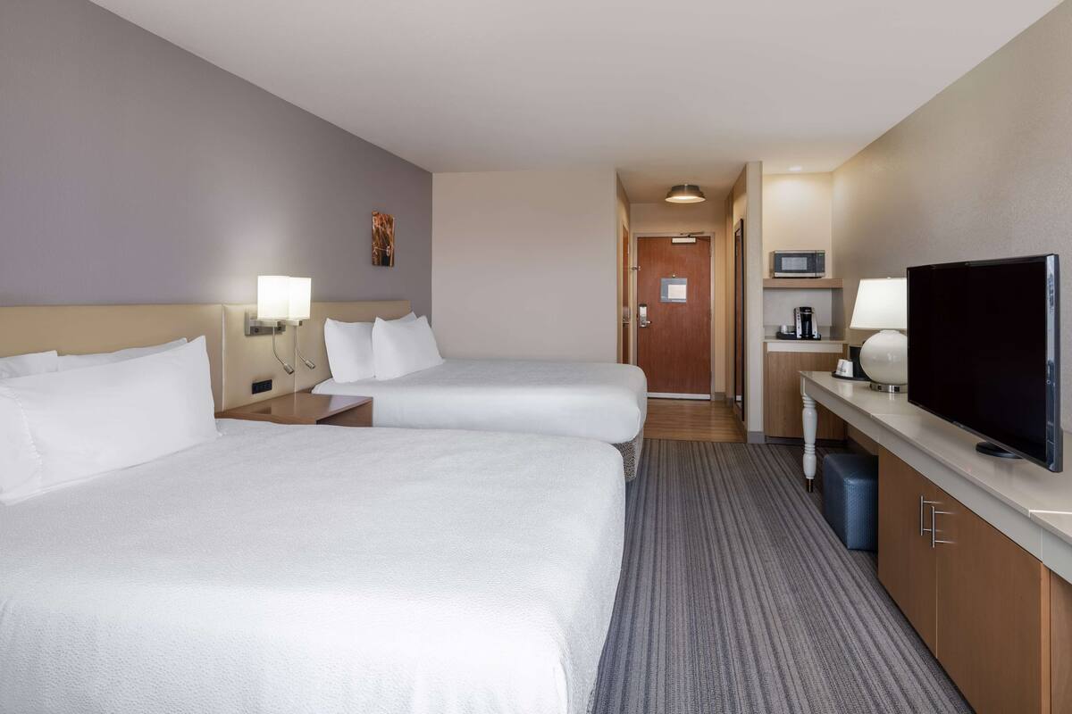 A hotel room with two beds, a TV, a microwave, and a small kitchenette.