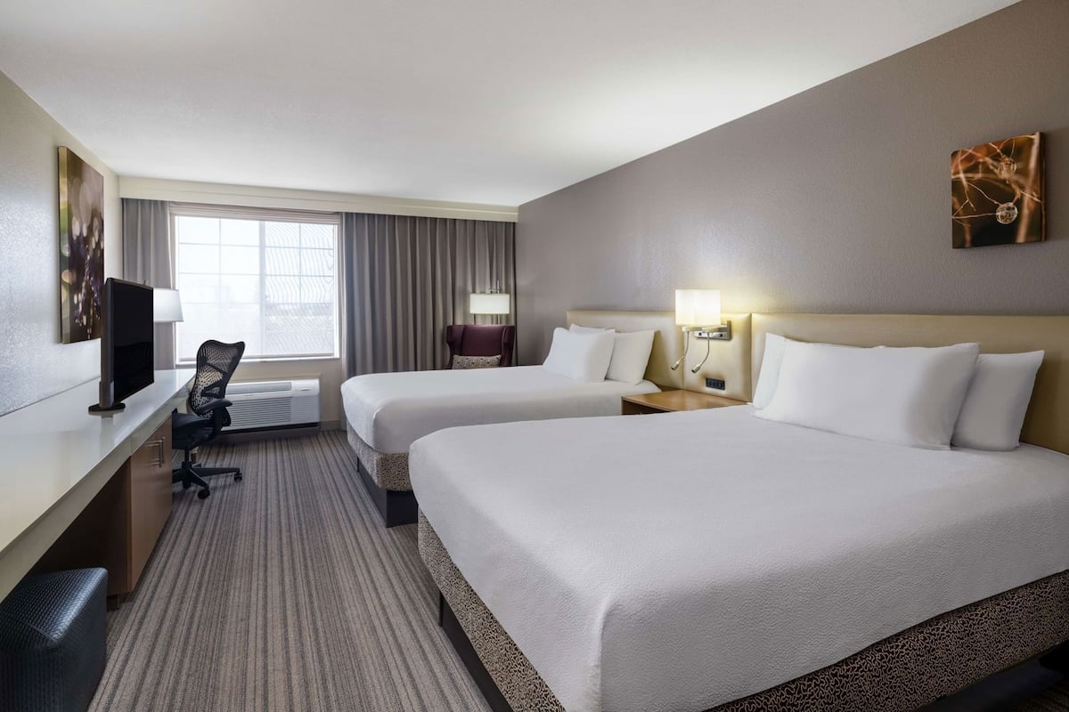 A hotel room with two beds, a desk, a chair, a TV, and a window with curtains.