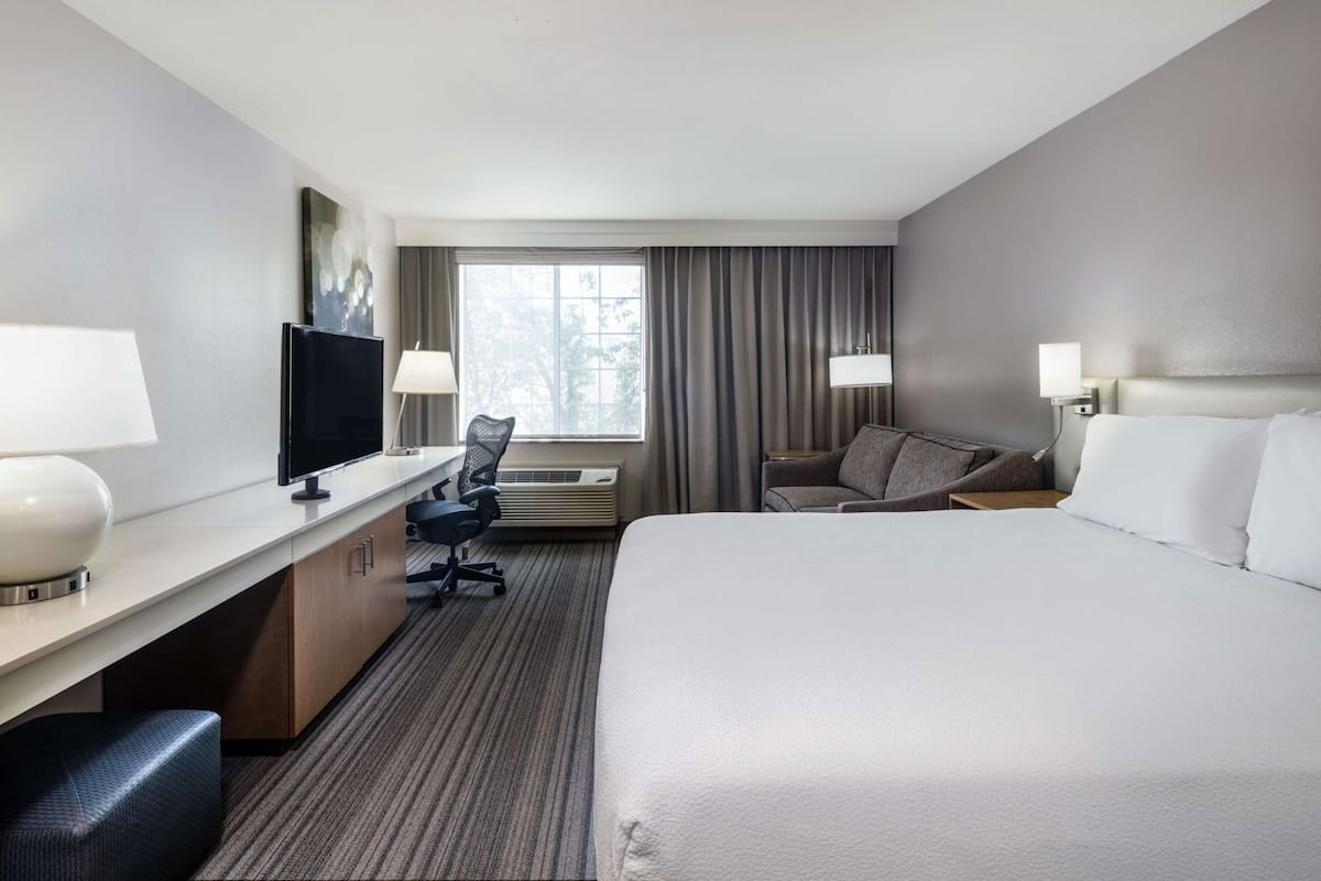 A hotel room with a bed, desk, chair, TV, and window with curtains.