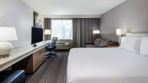 A hotel room with a bed, desk, chair, TV, and a window with curtains.