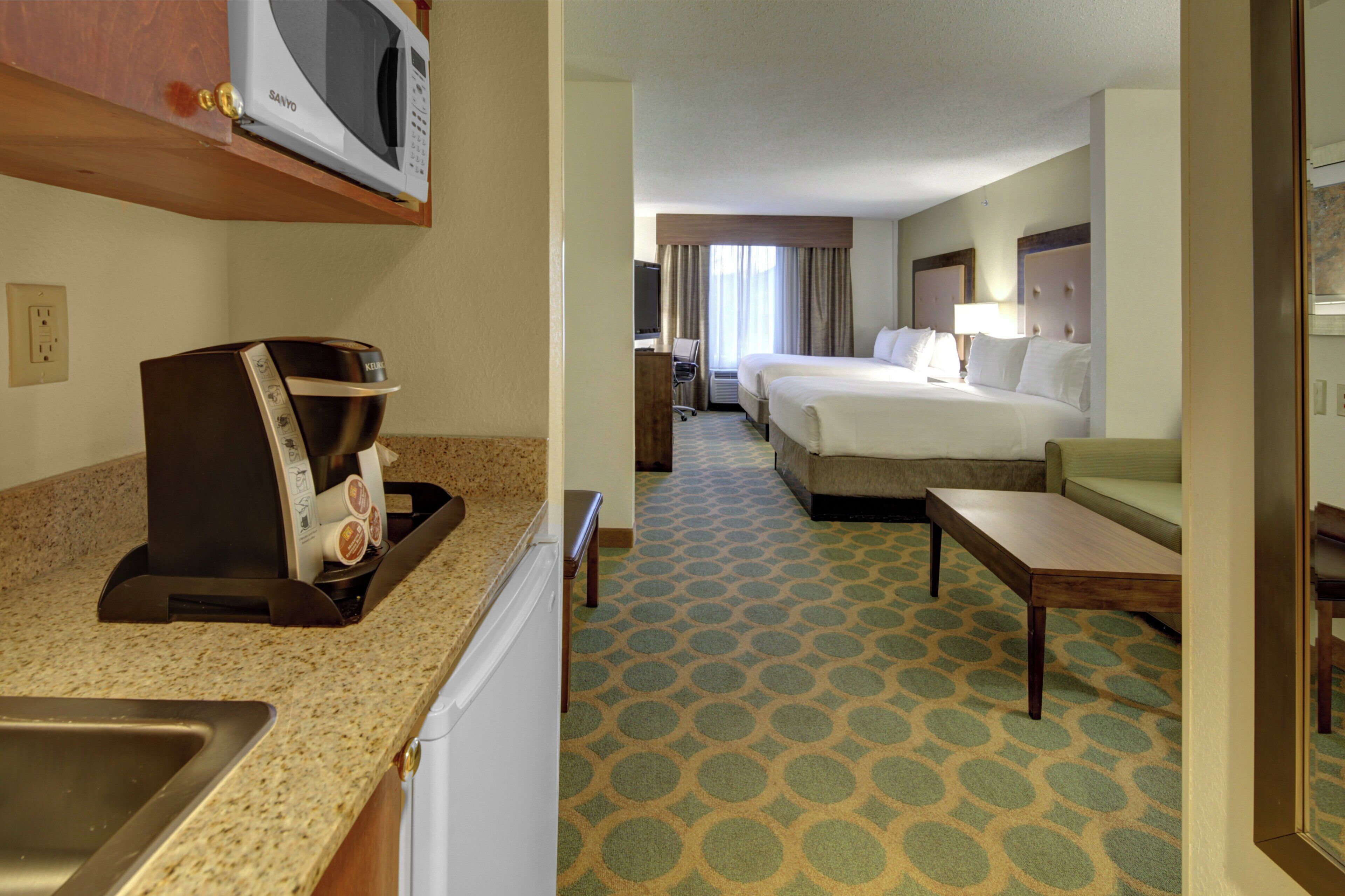 A hotel room with a kitchenette, a bed, a desk, and a television.