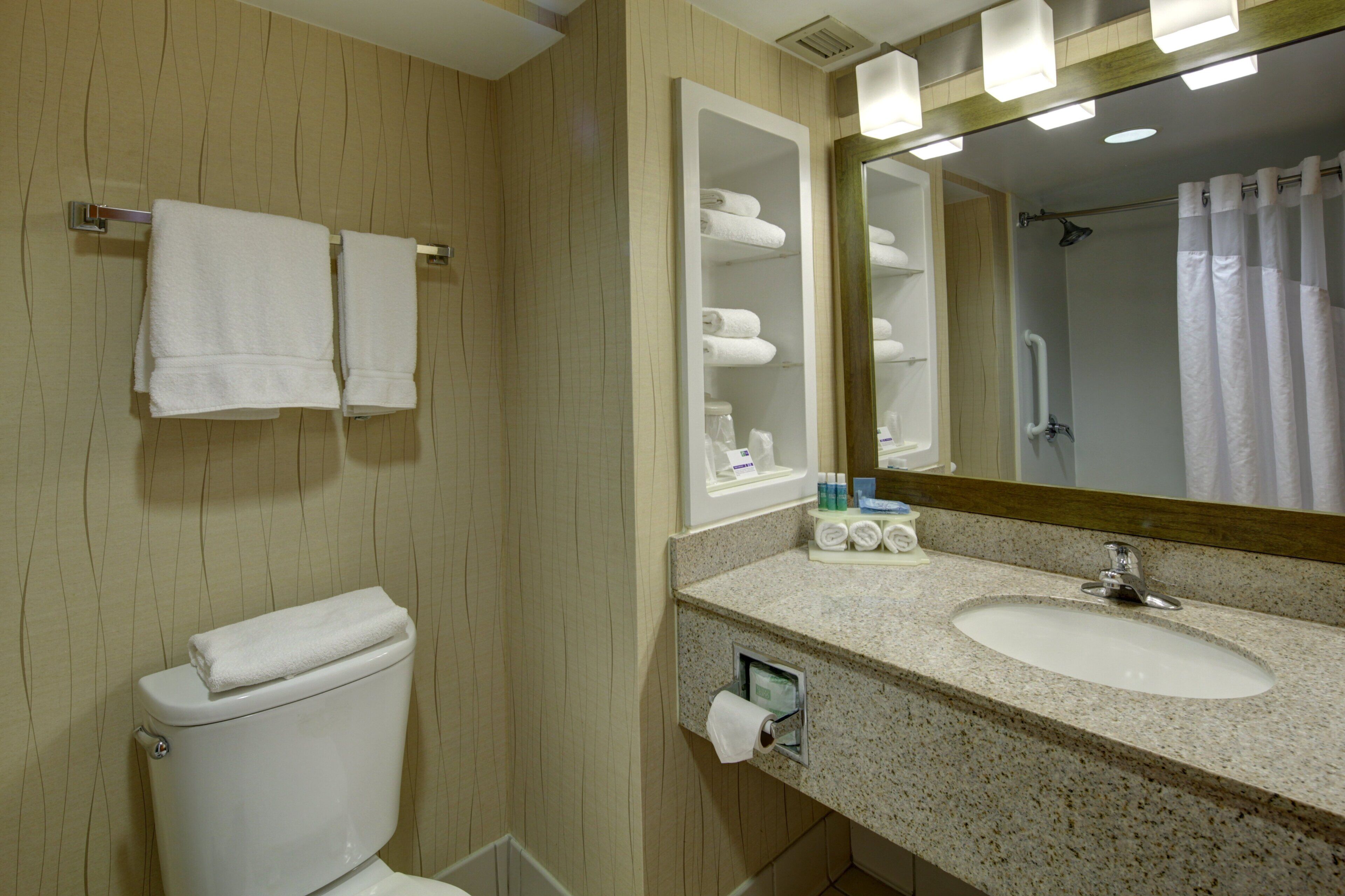 A bathroom with a toilet, sink, mirror, towel rack, and shower area.
