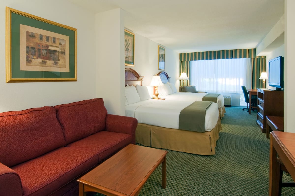 A hotel room with a red sofa, two beds, a desk, and a television.