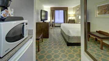 A hotel room with a microwave, a television, a bed, a desk, and a chair.