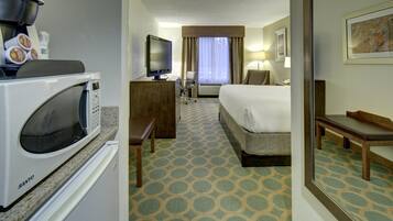 A hotel room with a kitchenette, a bed, a desk, a chair, and a television.