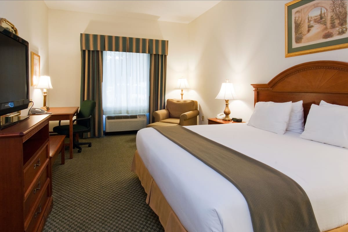 A hotel room with a large bed, a desk with a computer, a chair, a TV, and a painting on the wall.