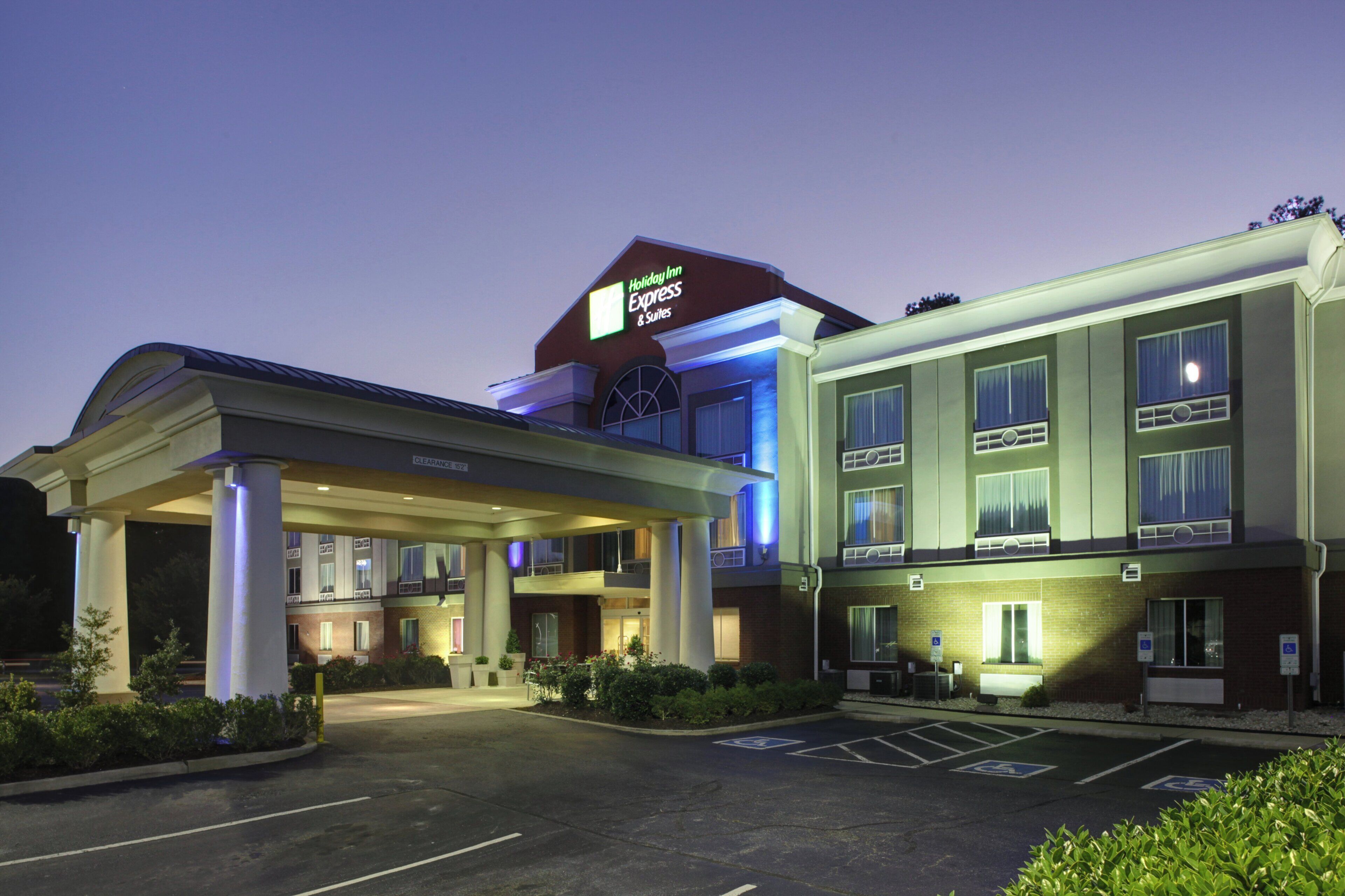 A Holiday Inn Express & Suites hotel with a covered entrance, multiple floors, and a parking lot with handicapped parking spaces.