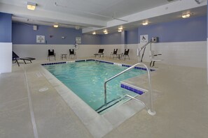 Ein Hallenbad mit blau-weißen Fliesen, einem Lifter für das Schwimmbecken und mehreren Liegestühlen rund um den Poolbereich.