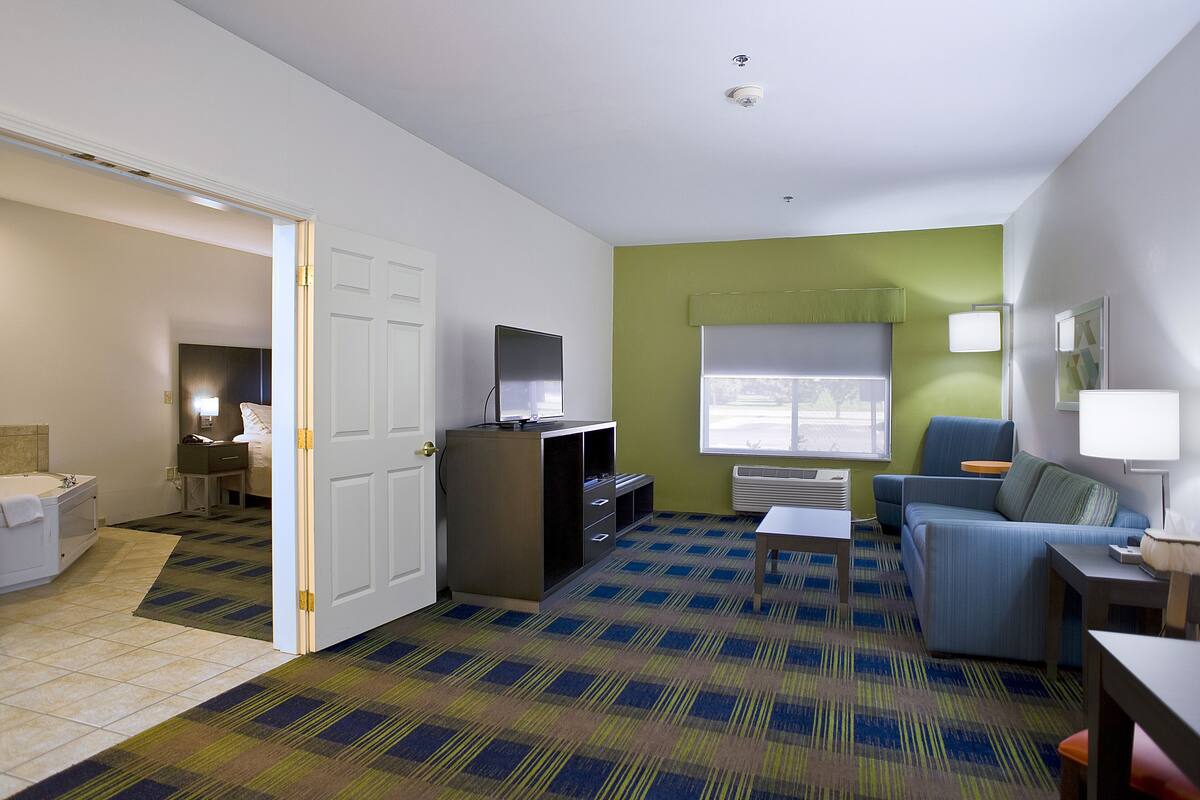 A hotel room with a bathroom, a living area with a sofa and a TV, and a patterned carpet.