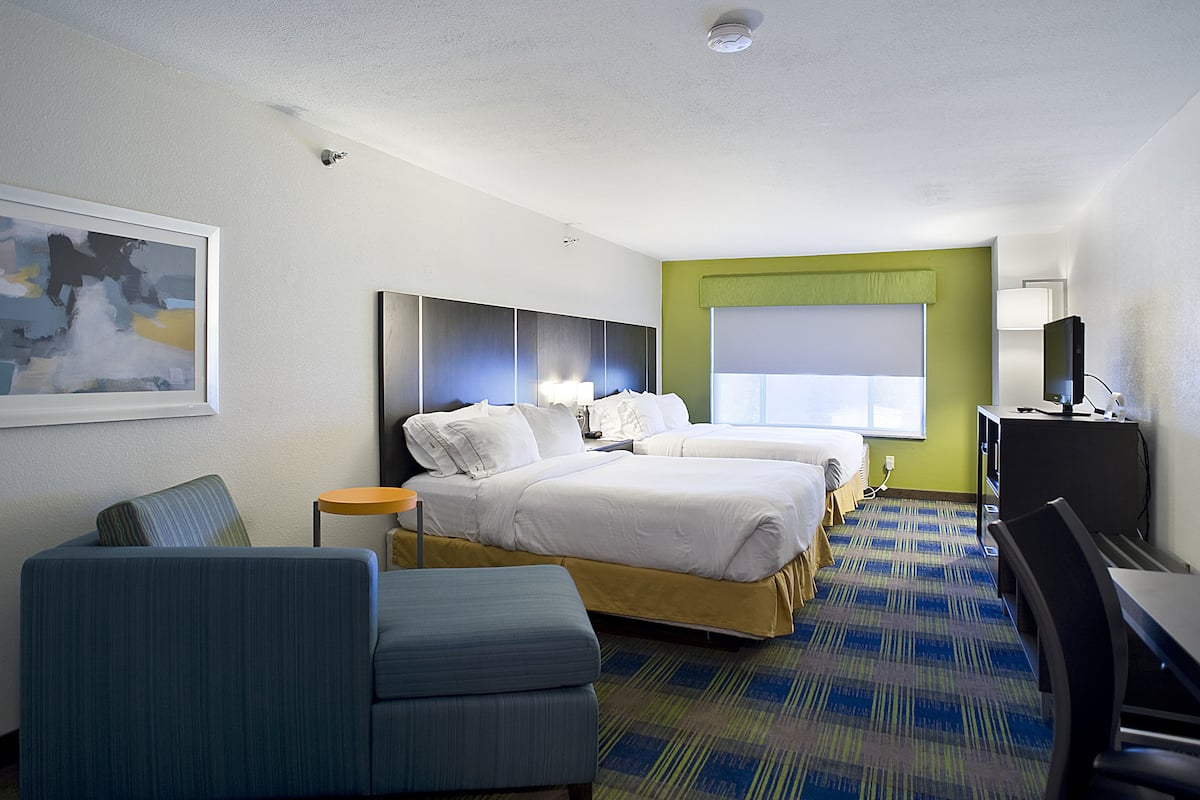 A hotel room with two beds, a desk, a chair, a TV, and a painting on the wall.