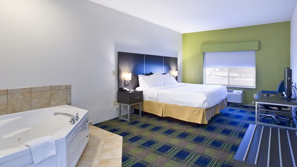 A hotel room with a large bed, a separate bathroom with a bathtub, a desk with a chair, and a window with blinds. - Holiday Inn Express Hotel & Suites Vermillion by IHG (Vermillion)