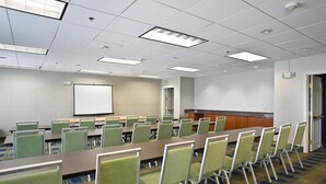 A conference room with a long table, multiple chairs, a projector screen, and a kitchen area. - Holiday Inn Express Hotel & Suites Vermillion by IHG (Vermillion)
