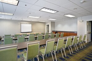 A conference room with a long table, multiple chairs, a projector screen, and a kitchen area. - Holiday Inn Express Hotel & Suites Vermillion by IHG (Vermillion)