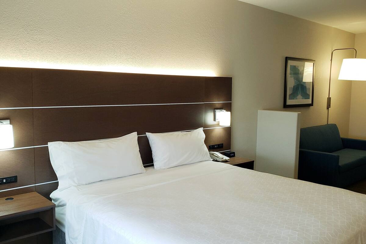 A hotel room with a large bed, two bedside tables, a desk, a chair, and a wall-mounted lamp.