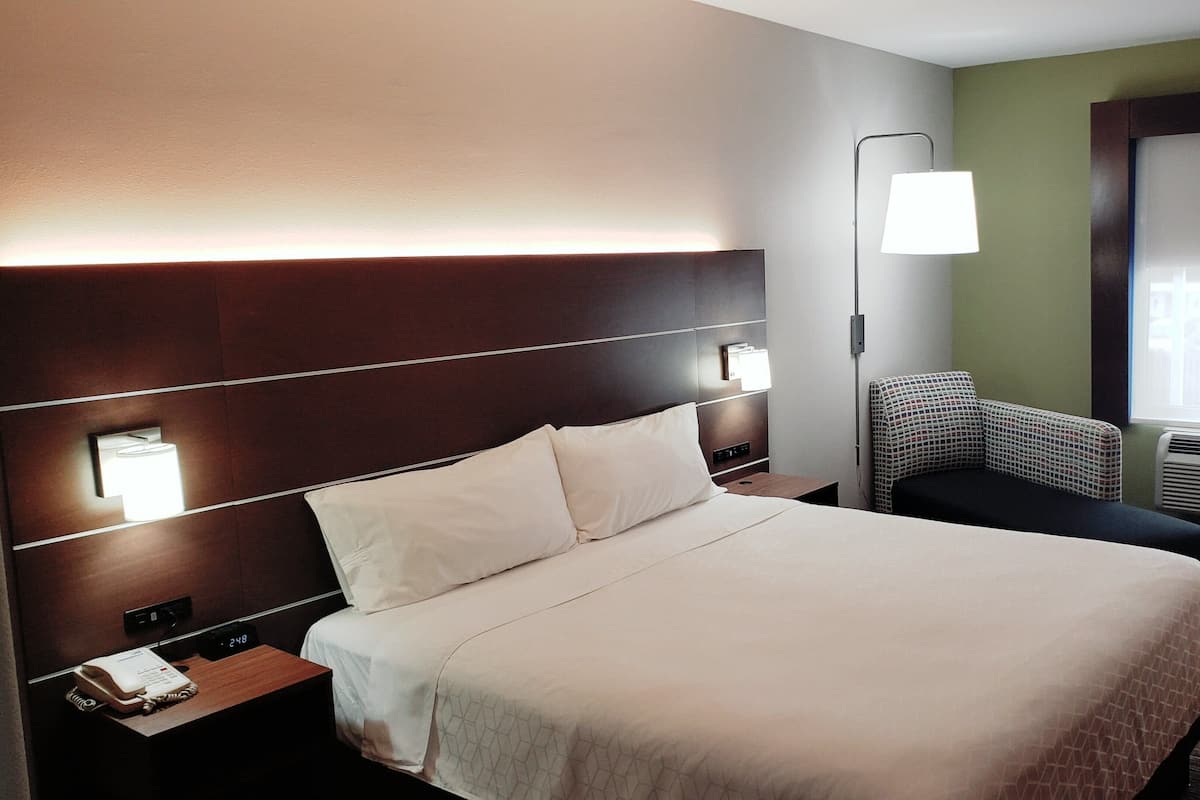 A hotel room with a large bed, bedside lamps, a chair, and a window with blinds.