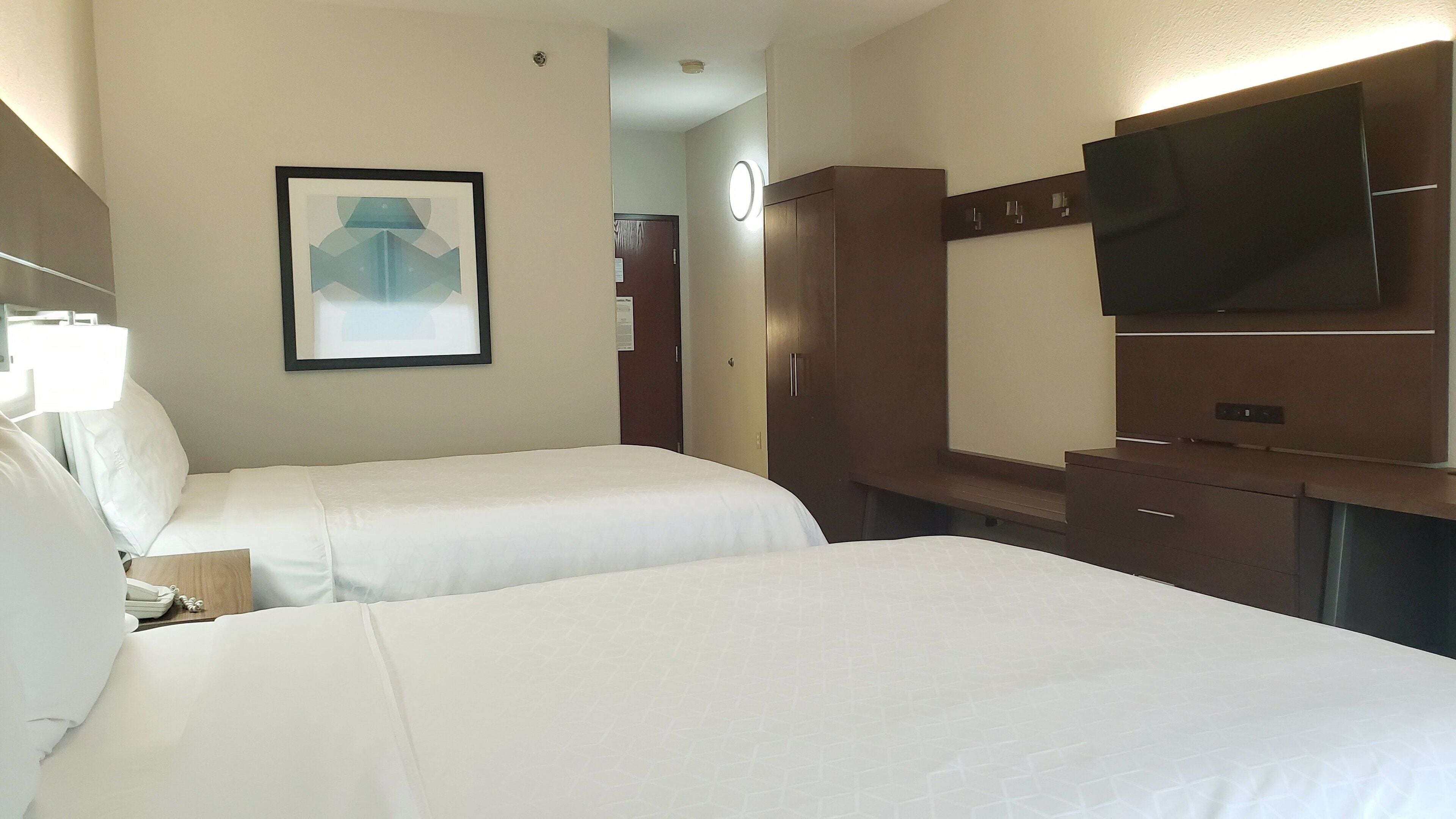 A hotel room with two beds, a TV, a desk, and a framed picture on the wall.