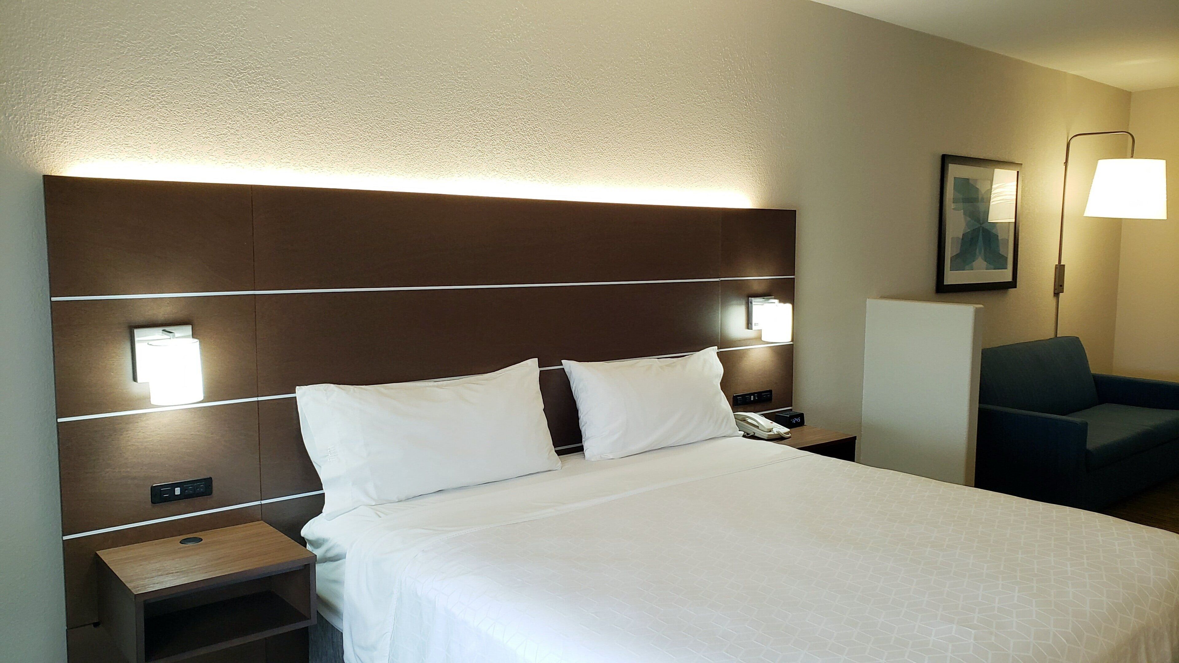 A hotel room with a large bed, bedside lamps, a desk, and a chair.