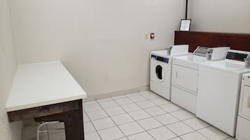 Un cuarto de lavandería con una mesa blanca, una lavadora, una secadora y un estante pequeño con un electrodoméstico blanco.