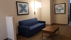 A hotel room with a blue sofa, a wooden coffee table, and two framed abstract artworks on the wall. - Holiday Inn Express Hotel & Suites Weslaco by IHG (Weslaco)